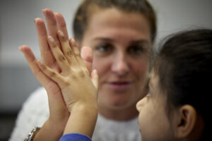 A teacher and a young child, pressing their palms together.