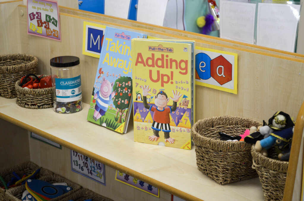 A book shelf in the classroom, with picture books, jars and basket with resources.