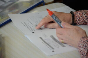 Hands pointing at printed classwork with a red marker pen.