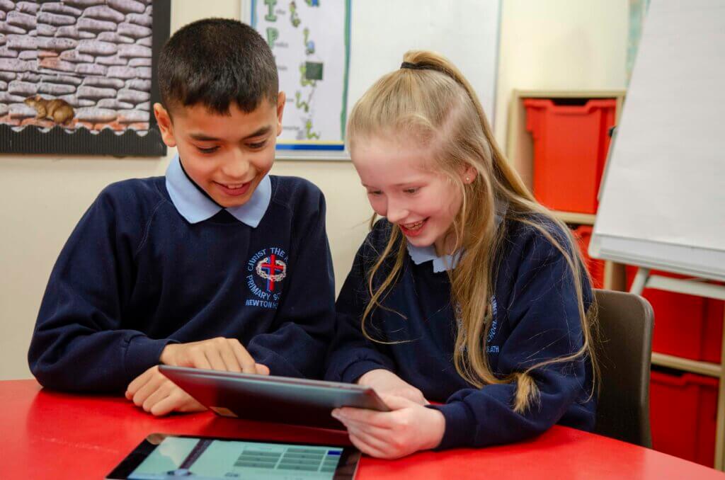 A boy and girl smiling whilst looking at a tablet in school.