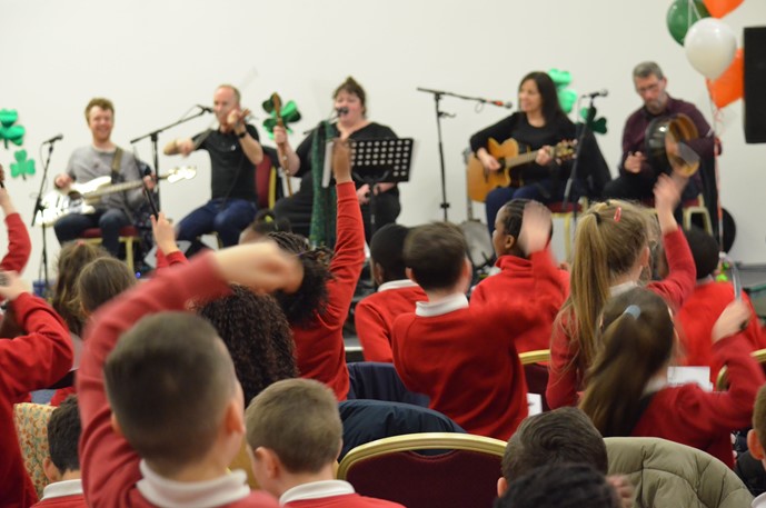 An audience of children dancing at the Irish Music Festival, as the musicians perform on stage. 