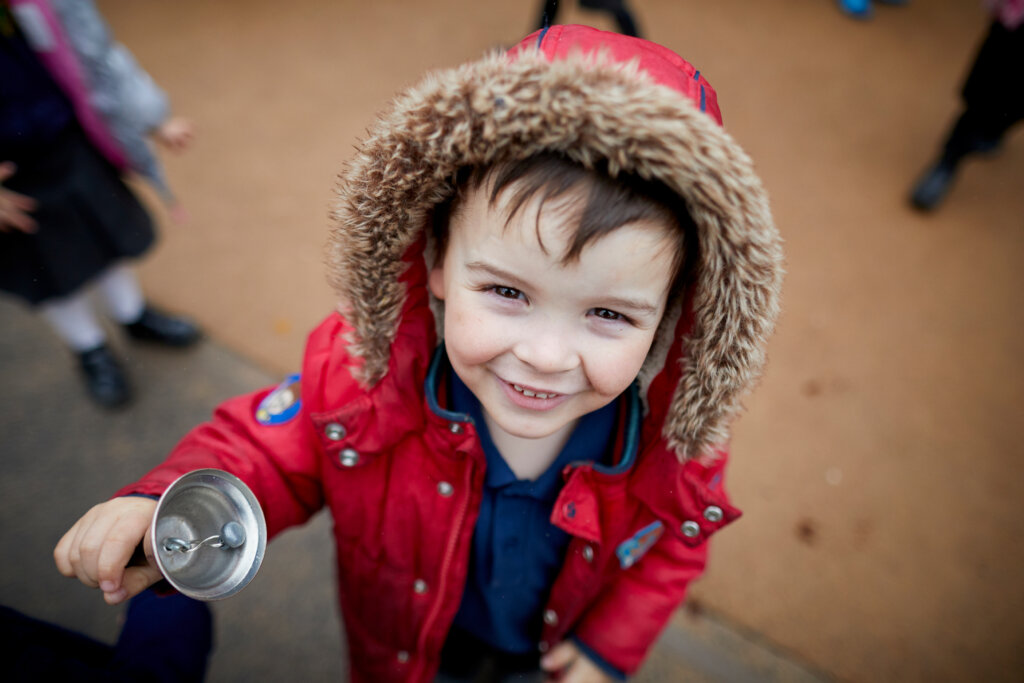 A young boy outdoors, wearing a red coat, smiling.