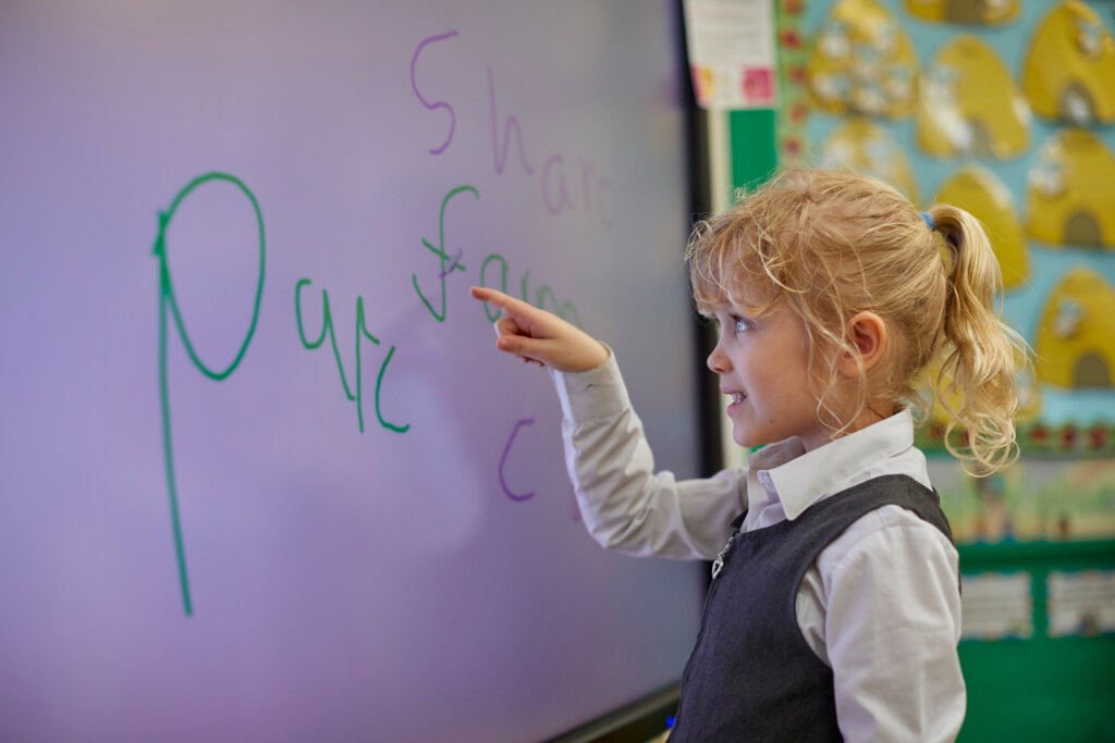 A girl practicing writing letters on the whiteboard.