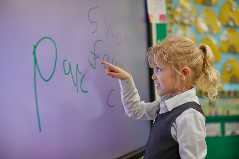 A girl practicing writing letters on the whiteboard.