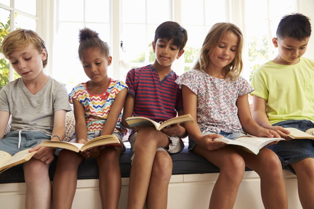 Five children sitting on a windowsill and reading books.