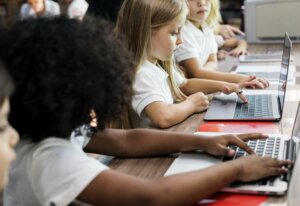 School girls sitting at a table and typing on their laptops.