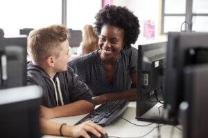 A teacher and pupil smiling in front of a computer.