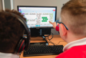 Two pupils sitting in front of a computer, one points at the screen.