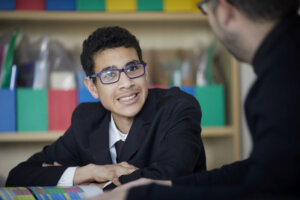 A teenage boy in school uniform, smiling towards his teacher.