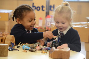 Two girl pupils playing with plastic farm animals