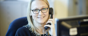 A woman sitting at her desk, smiling as she holds a telephone.