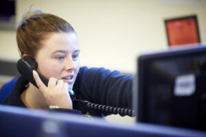 A woman sitting in front of a computer whilst on the telephone.