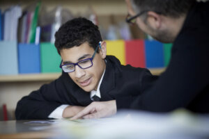 A student looks at something on his desk where his teacher his pointing.