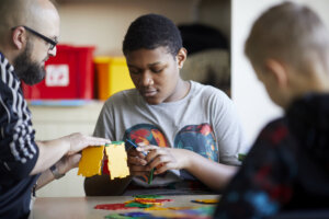 A student putting together a toy structure whilst his teacher helps.