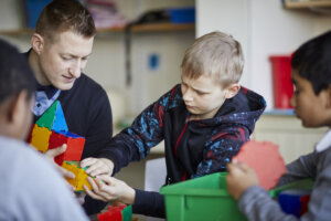 A boy playing with a plastic toy structure, whilst his teacher helps.