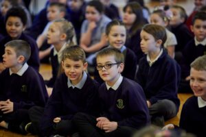 Children sitting on the floor of the school hall, gathered for an assembly.