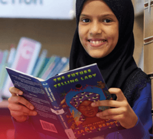 A girl smiling whilst she reads a book.