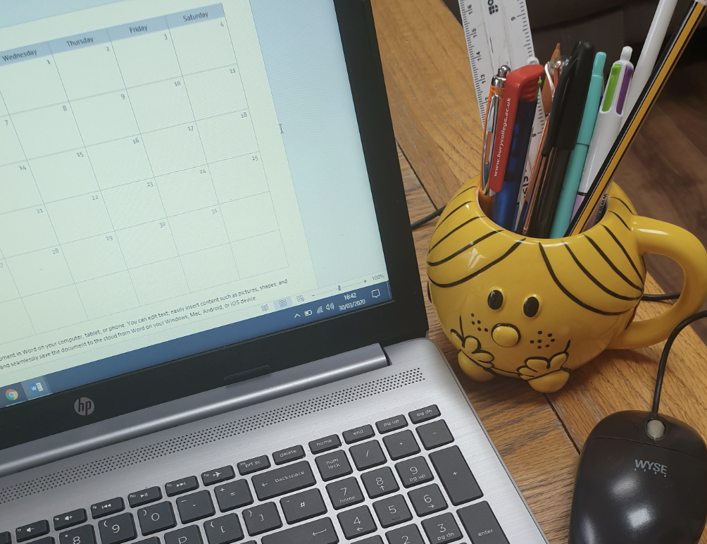 An open laptop with a Little Miss Sunshine mug beside it, full of pens, pencils and rulers.